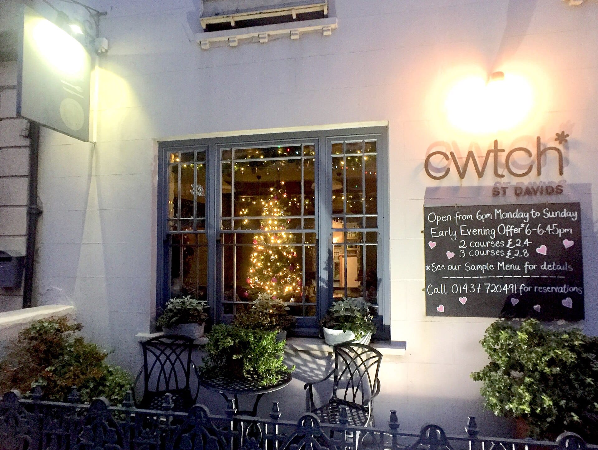 Front of Cwtch restaurant on St Davids High Street lit up in the evening with plants outside