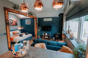 Open-plan living area at Tŷ Cosy with sofa, log burner and double bed beyond, St Davids