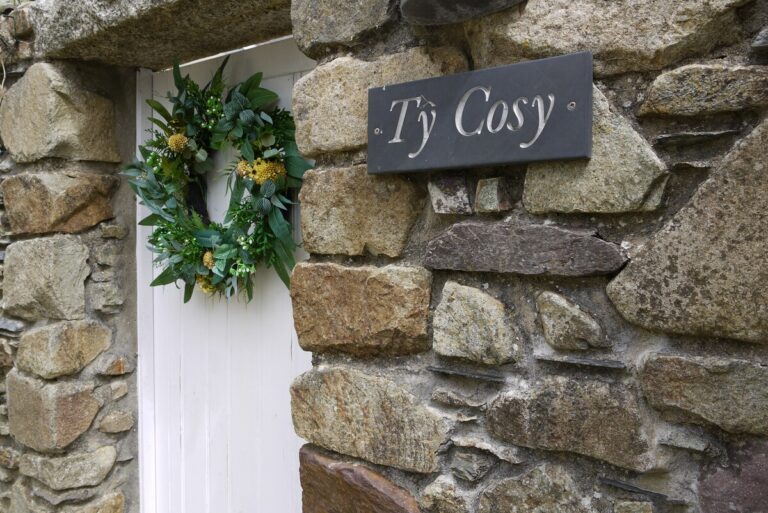 Slate Tŷ Cosy name sign and wreath on the stone wall by the cottage door