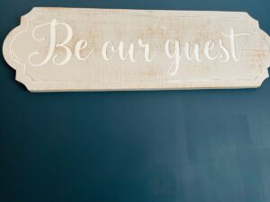 Hand-painted 'Be our guest' sign on a navy wall at Tŷ Cosy
