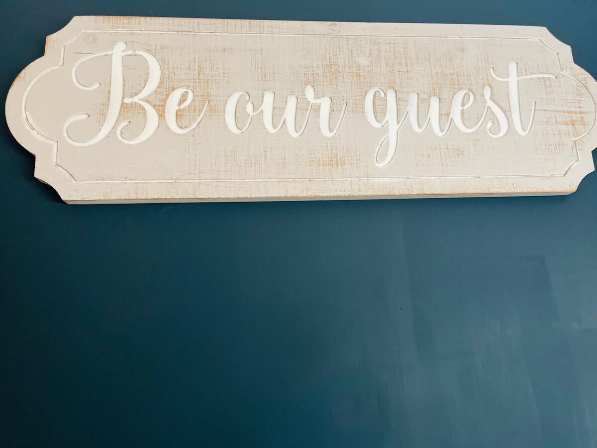 Hand-painted 'Be our guest' sign on a navy wall at Tŷ Cosy