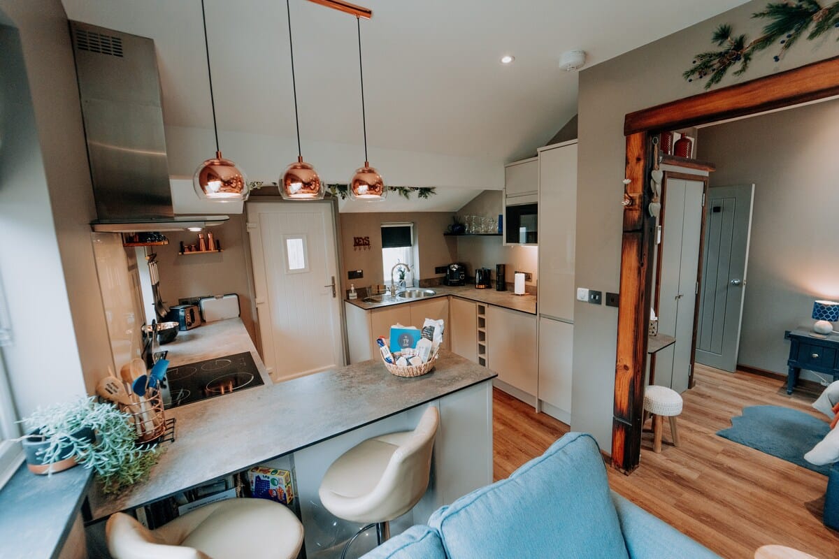 Tŷ Cosy kitchen with breakfast bar and copper pendant lights, opening onto the living area